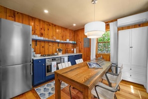 A kitchen with wooden walls, a stainless steel refrigerator, a stove, and a dining table with chairs.