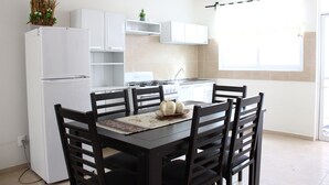 A modern kitchen with white cabinets, a dining table with chairs, a refrigerator, and a window with a curtain. - Casa Blanca Oaxaca (Oaxaca)