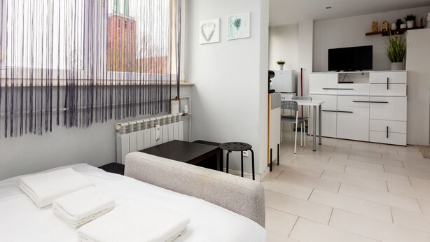 A modern hotel room with a bed, a desk, and a kitchenette.