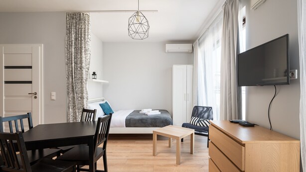 Uma sala de estar moderna com uma mesa de jantar de madeira, cadeiras, um sofá, uma TV fixada na parede e um armário de madeira.