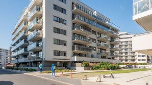 Um edifício residencial com vários andares, varandas, um pátio pavimentado e um céu azul claro.