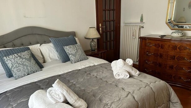 A neatly made bed with a grey quilt, two rolled towels, and a wooden dresser with drawers. - Spacious, centrally located home, very close to the subway (Napoli)