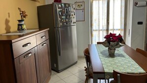 A kitchen with a refrigerator, wooden cabinets, a dining table with chairs, and a vase with flowers. - Spacious, centrally located home, very close to the subway (Napoli)