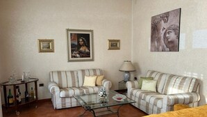 A living room with two striped sofas, a glass coffee table, and a yellow sofa. There are framed pictures on the walls and a lamp on a side table. - Spacious, centrally located home, very close to the subway (Napoli)