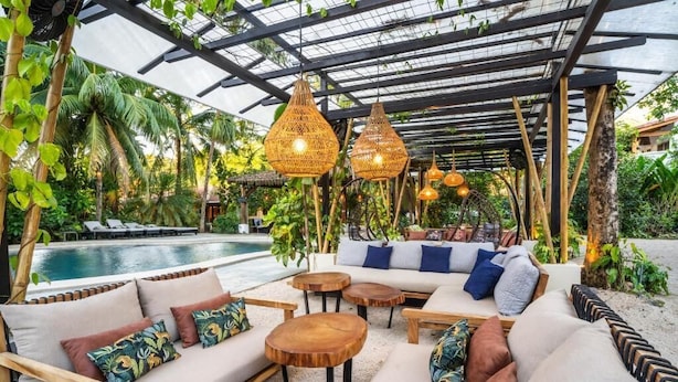 An outdoor lounge area with a pool, wooden furniture, and hanging rattan lights. - Curiol Boutique Hotel & Lounge (Tempate)