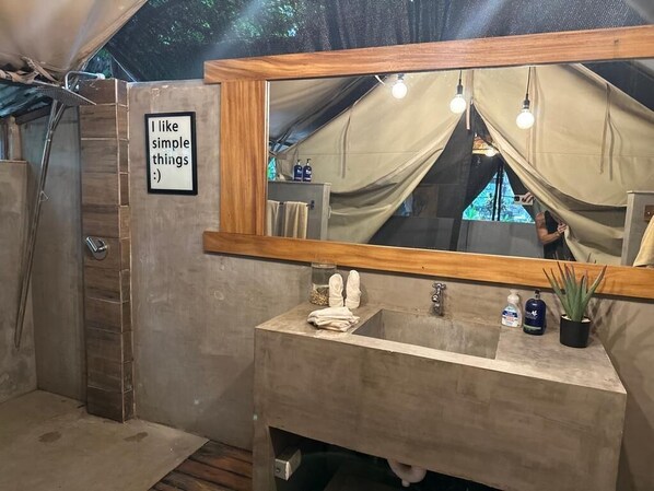 Un baño con espejo de marco de madera, lavamanos y perchero. Un cartel en la pared dice 'Me gustan las cosas sencillas :).'