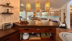 A modern kitchen with a central island, hanging woven light fixtures, and a view of the outdoors through large windows. - Curiol Boutique Hotel & Lounge (Tempate)