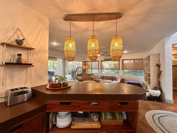 Cocina moderna con una isla central, lámparas colgantes tejidas y vistas al exterior a través de amplios ventanales.