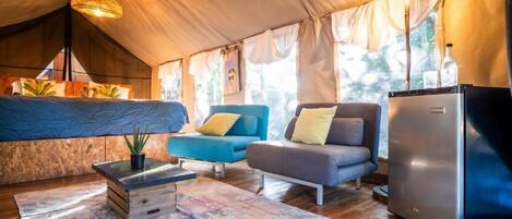 A cozy tented accommodation with a bed, two sofas, a refrigerator, and a hanging light fixture.