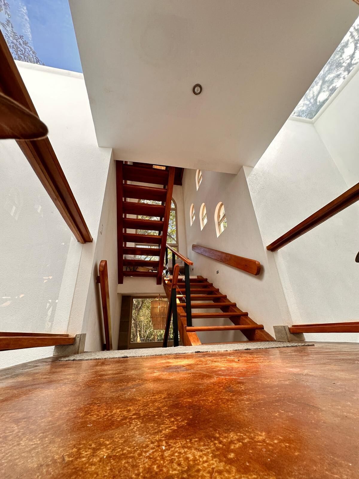 A modern interior with a wooden staircase, white walls, and a ceiling light.