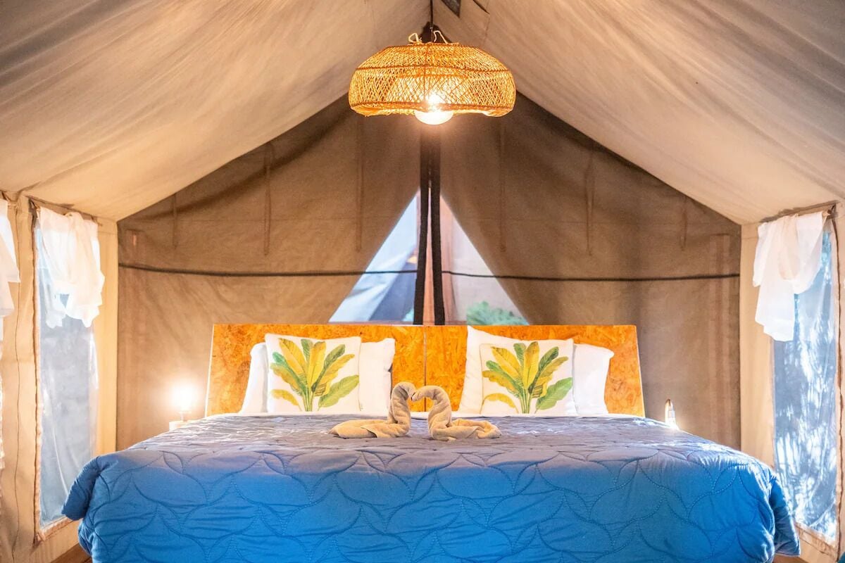 A tented room with a bed, a hanging light fixture, and a window with curtains.