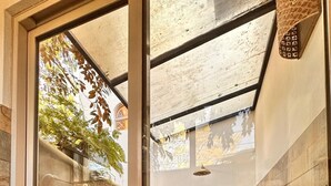 A glass door leading to a patio area with stone flooring, a hanging plant, and a view of trees through the glass. - Curiol Boutique Hotel & Lounge (Tempate)