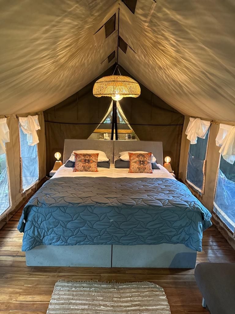A tent-style bedroom with a bed, pillows, a hanging light fixture, and a nightstand.