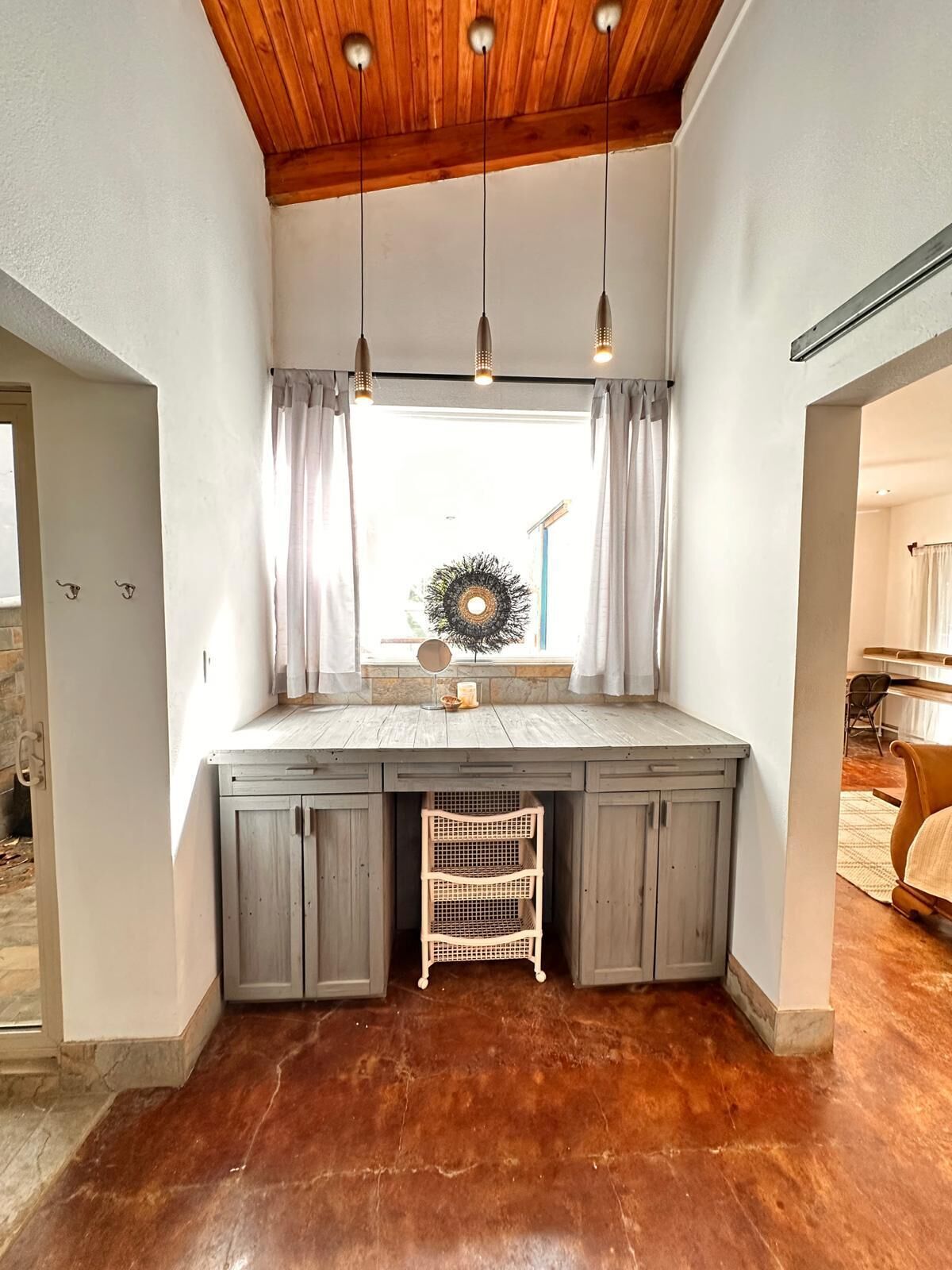Una habitación acogedora con techo de madera, un banco empotrado con espacio de almacenamiento, una ventana con cortinas y una lámpara colgante.