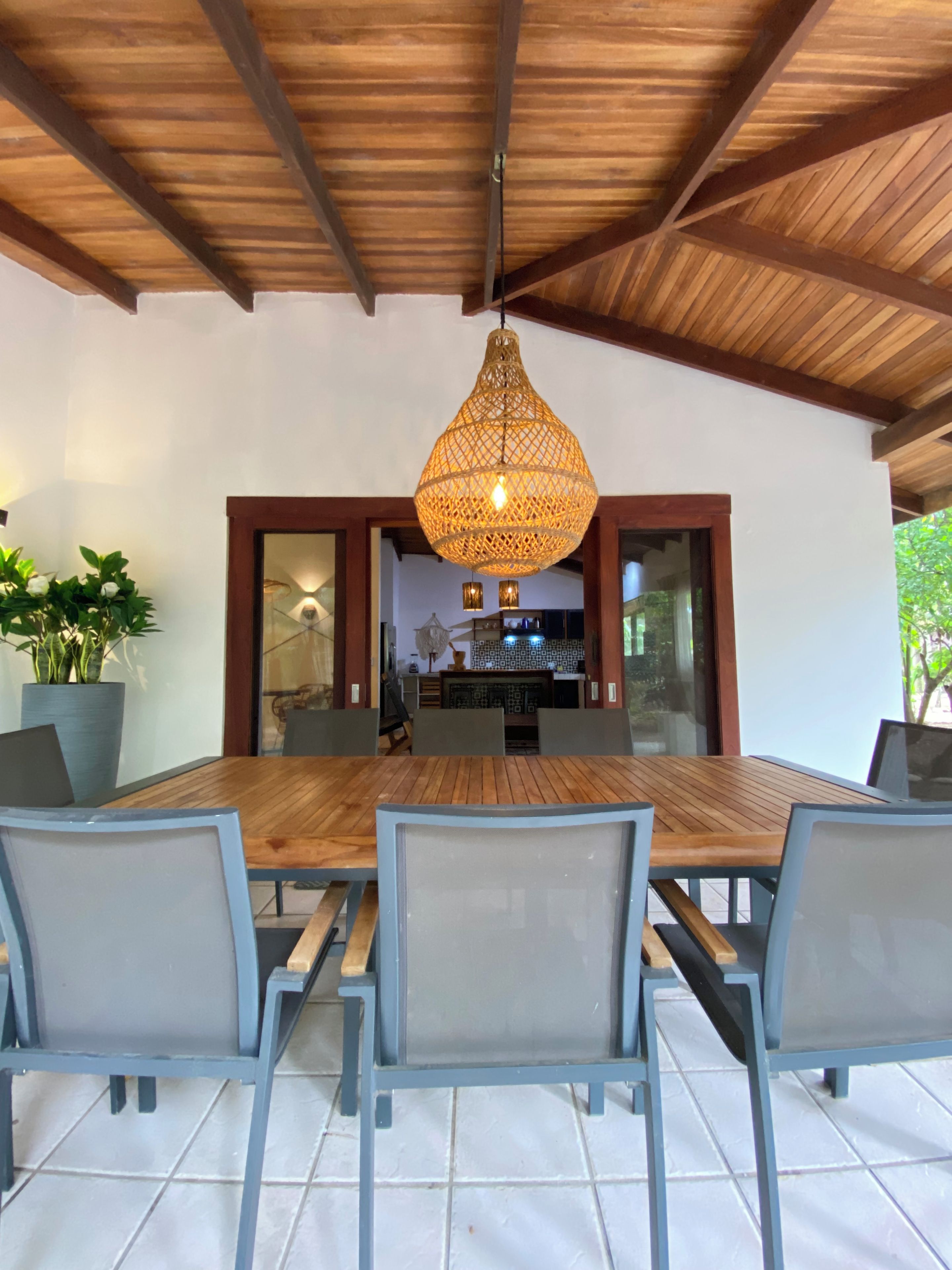 Un comedor con una mesa y sillas de madera, una lámpara colgante y vista a la cocina.