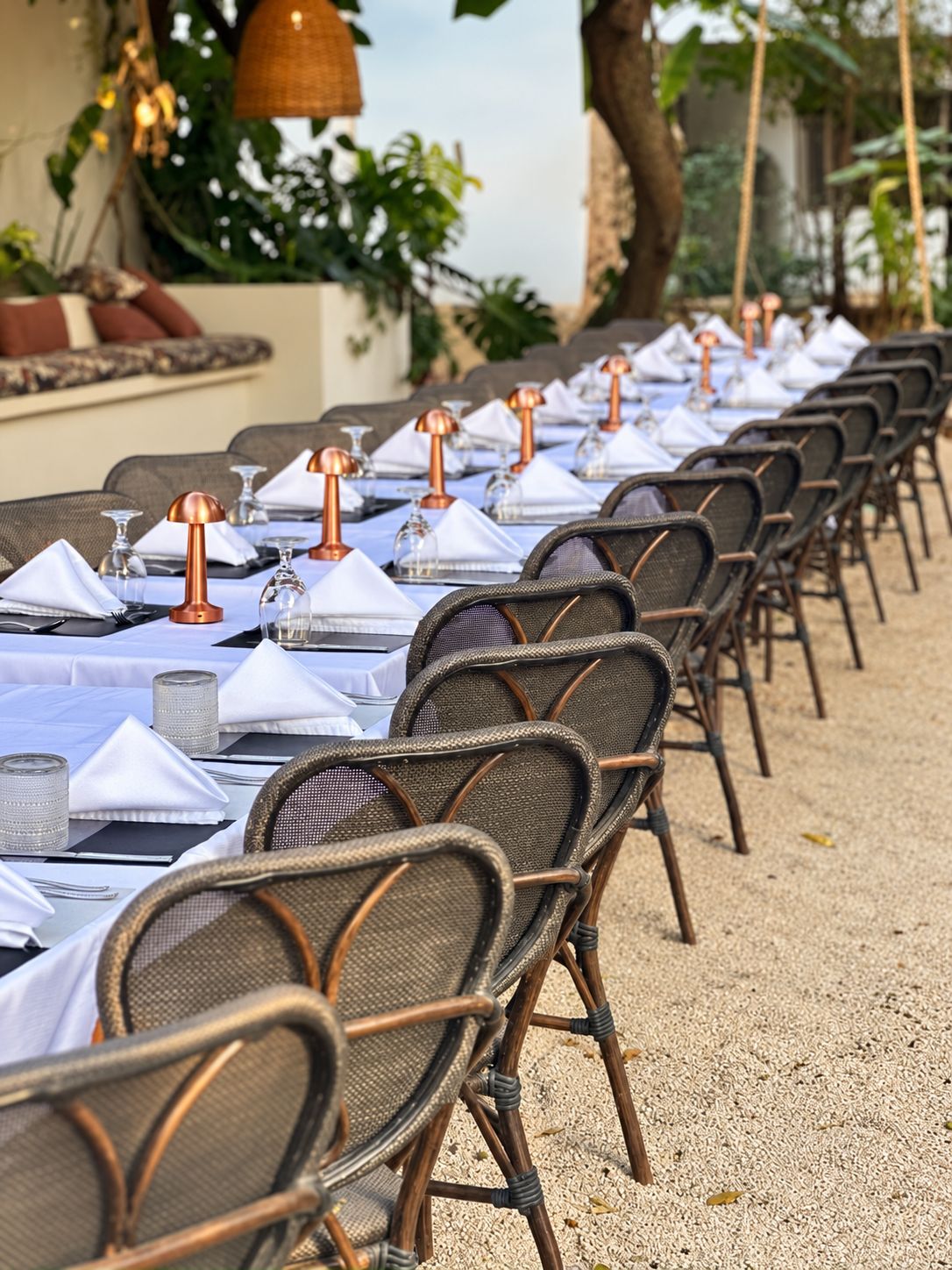 Una larga mesa de comedor con sillas, manteles blancos y candelabros de cobre.