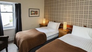 A hotel room with two beds, a window with curtains, a framed picture on the wall, and a checkered wall pattern.