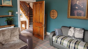 A cozy living room with a plaid sofa, a leather armchair, and a wooden door leading to a staircase.