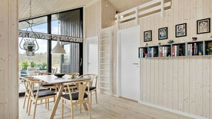 A dining area with a wooden table and chairs, a bookshelf with books and decorative items, and a view through a large window. - Nice home in Ejstrupholm with kitchen (Ejstrupholm)