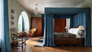 Un dormitorio con cama de dos columnas, suelo de madera, un candelabro y vistas al exterior.