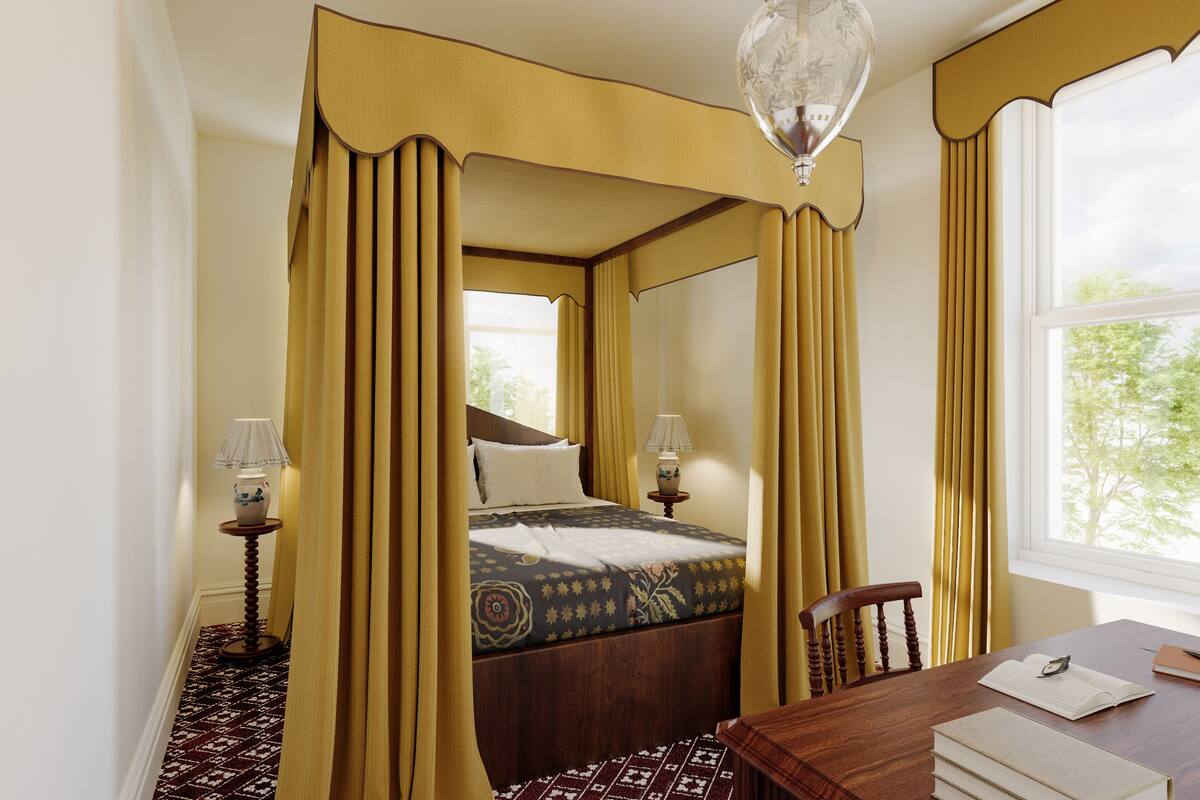 A four-poster bed with curtains, a wooden table with books and a pen, and a window with a view of trees.