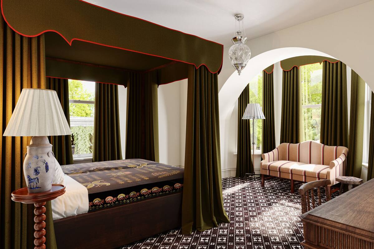 A bedroom with a four-poster bed, a sofa, a wooden table, and a lamp.