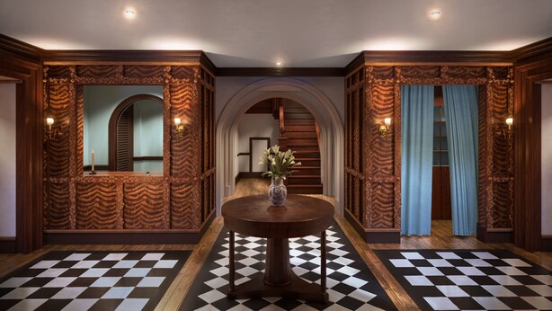 Una habitación con piso a cuadros, una mesa redonda de madera con un florero y paneles de madera ornamentales en las paredes.