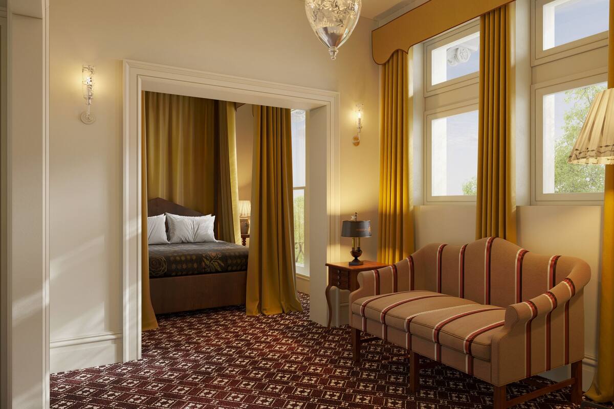 A hotel room with a bed, a sofa, a lamp, and a patterned carpet.