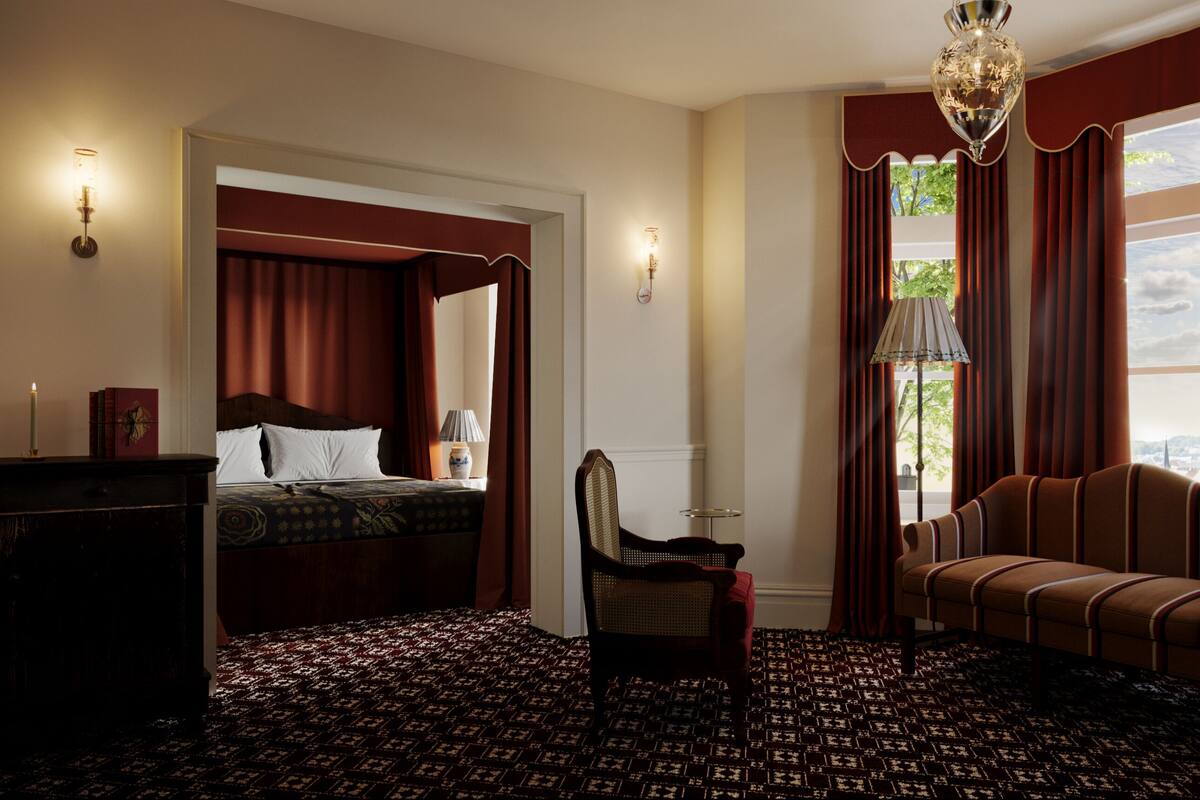 A hotel room with a bed, a chair, a desk, and a lamp. There is a window with curtains and a view of the outside.