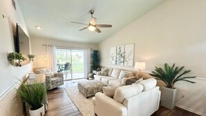 A spacious living room with a ceiling fan, a large sofa set, a coffee table, and a dining area with a table and chairs. - Cozy Coastal Retreat, Steps to the Sugar Sand Beach of FMB! (Fort Myers Beach)