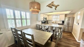 A modern kitchen with a dining area, large windows, and a hanging light fixture. - Cozy Coastal Retreat, Steps to the Sugar Sand Beach of FMB! (Fort Myers Beach)