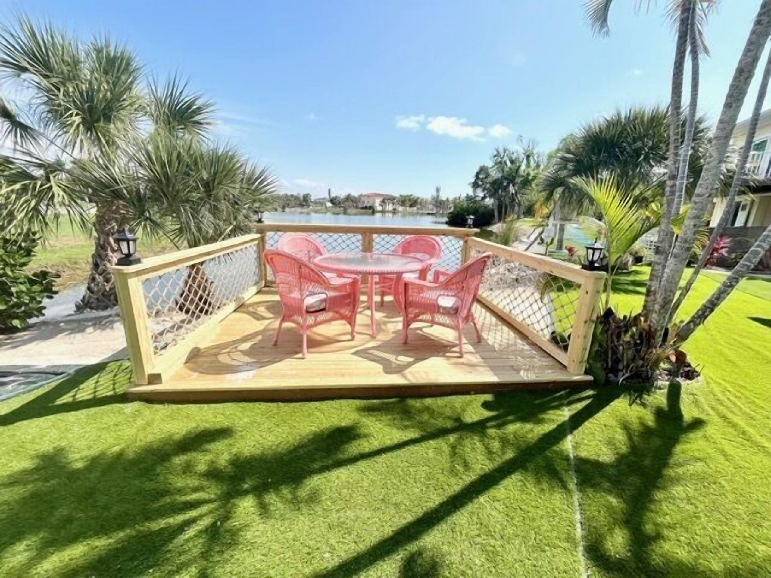 A deck with a table and chairs, surrounded by a fence, overlooking a pool and palm trees.
