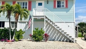 A two-story house with a white exterior, red shutters, and a small balcony. - Cozy Coastal Retreat, Steps to the Sugar Sand Beach of FMB! (Fort Myers Beach)