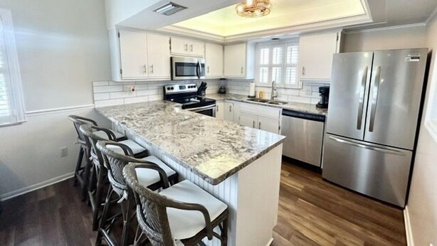 A modern kitchen with a marble island, stainless steel appliances, and a bar area with chairs. - Cozy Coastal Retreat, Steps to the Sugar Sand Beach of FMB! (Fort Myers Beach)