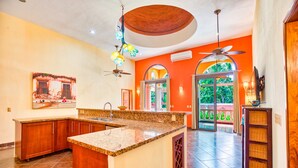 A kitchen with granite countertops, wooden cabinets, and a central island. There is a ceiling fan, a hanging light fixture, and a window with a view of greenery outside. - Gorgeous Hacienda-style, private Casa de Paz, with 24-hour gated security (Bucerias)