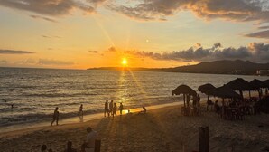 A beach scene with people walking and sitting, umbrellas, and a sunset over the ocean. - Gorgeous Hacienda-style, private Casa de Paz, with 24-hour gated security (Bucerias)