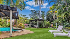 A pool area with lounge chairs, a covered seating area, and lush tropical vegetation. - Balgal Beach Units (Balgal Beach)