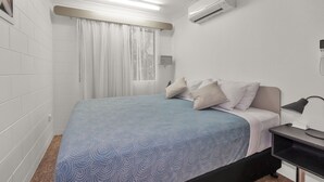 A bedroom with a bed, a nightstand, an air conditioner, and a window with curtains. - Balgal Beach Units (Balgal Beach)