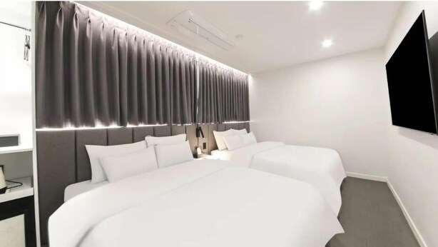 A modern hotel room with two beds, a bedside table, a lamp, and a large window with curtains. - JI STAY Hotel Gyeongju (Gyeongju)