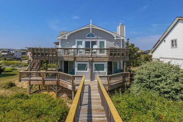 Une maison à deux étages dotée d’un balcon et d’une terrasse en bois menant à l’entrée.