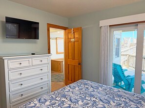 Une chambre à coucher avec un lit, une commode, un téléviseur, une porte en bois et une vue sur un balcon avec des chaises.