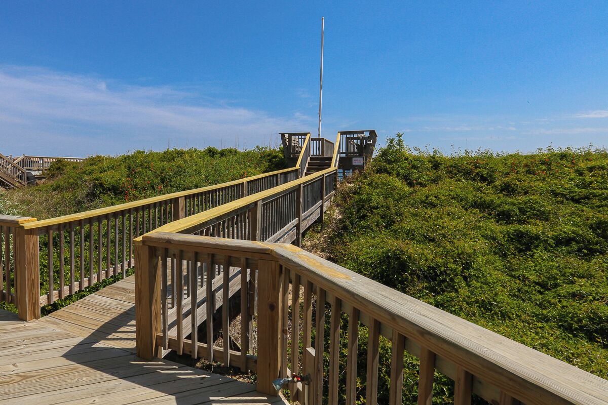 A wooden boardwalk leading to a lookout point with a flagpole, surrounded by greenery.