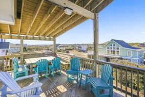 Une terrasse en bois avec des sièges extérieurs, offrant une vue sur une zone côtière avec des maisons.