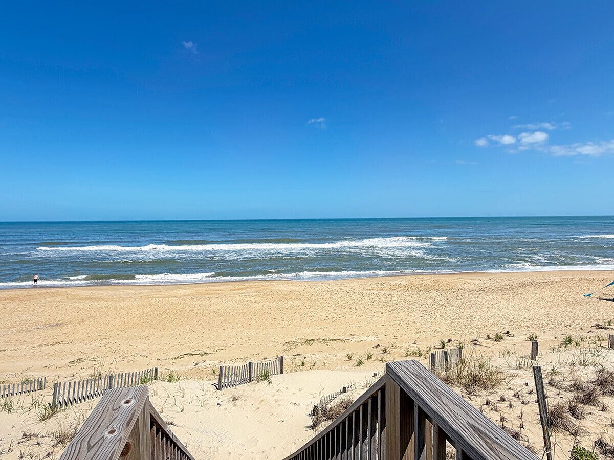 A beach with a wooden boardwalk leading to the water, a sandy beach, and the ocean.