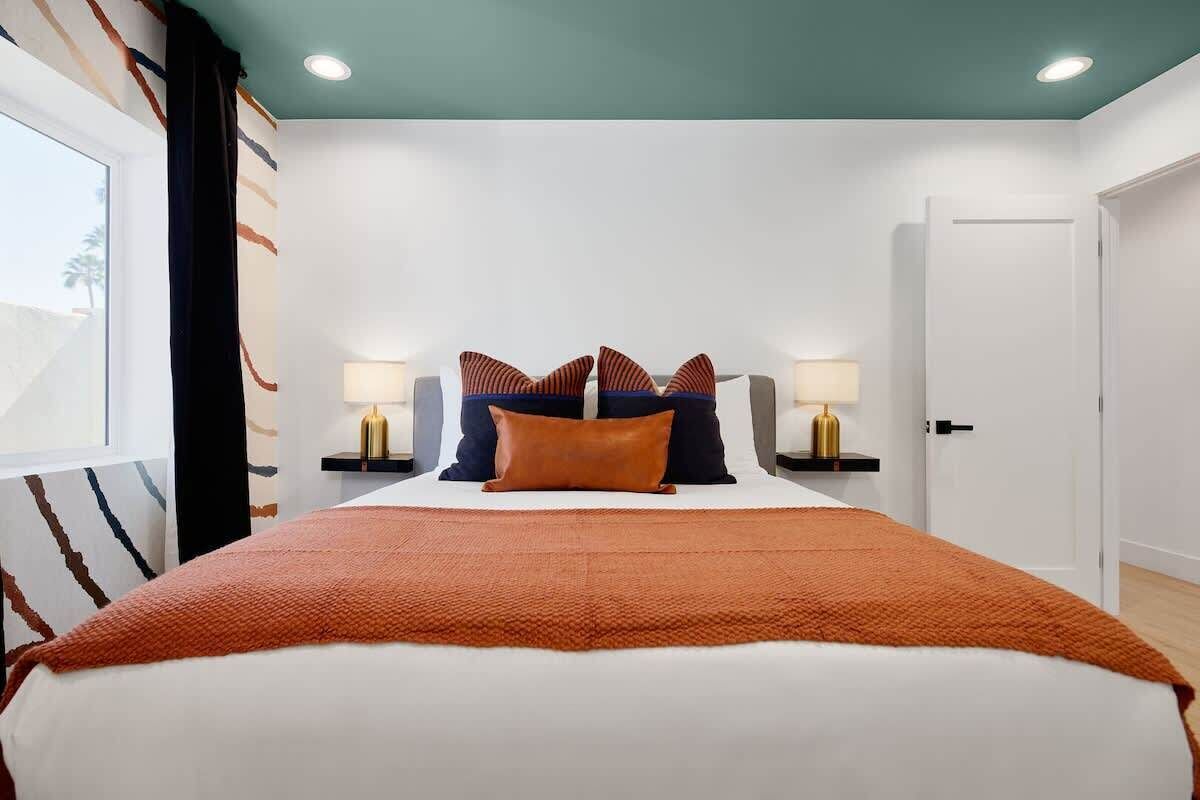 A bedroom with a bed, two bedside tables, a nightstand, a window with curtains, and a door.