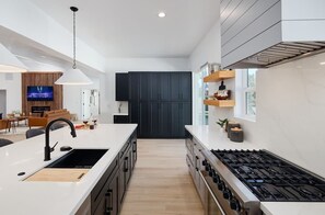 Una cocina moderna con una isla central, armarios negros, una estufa y un televisor al fondo.