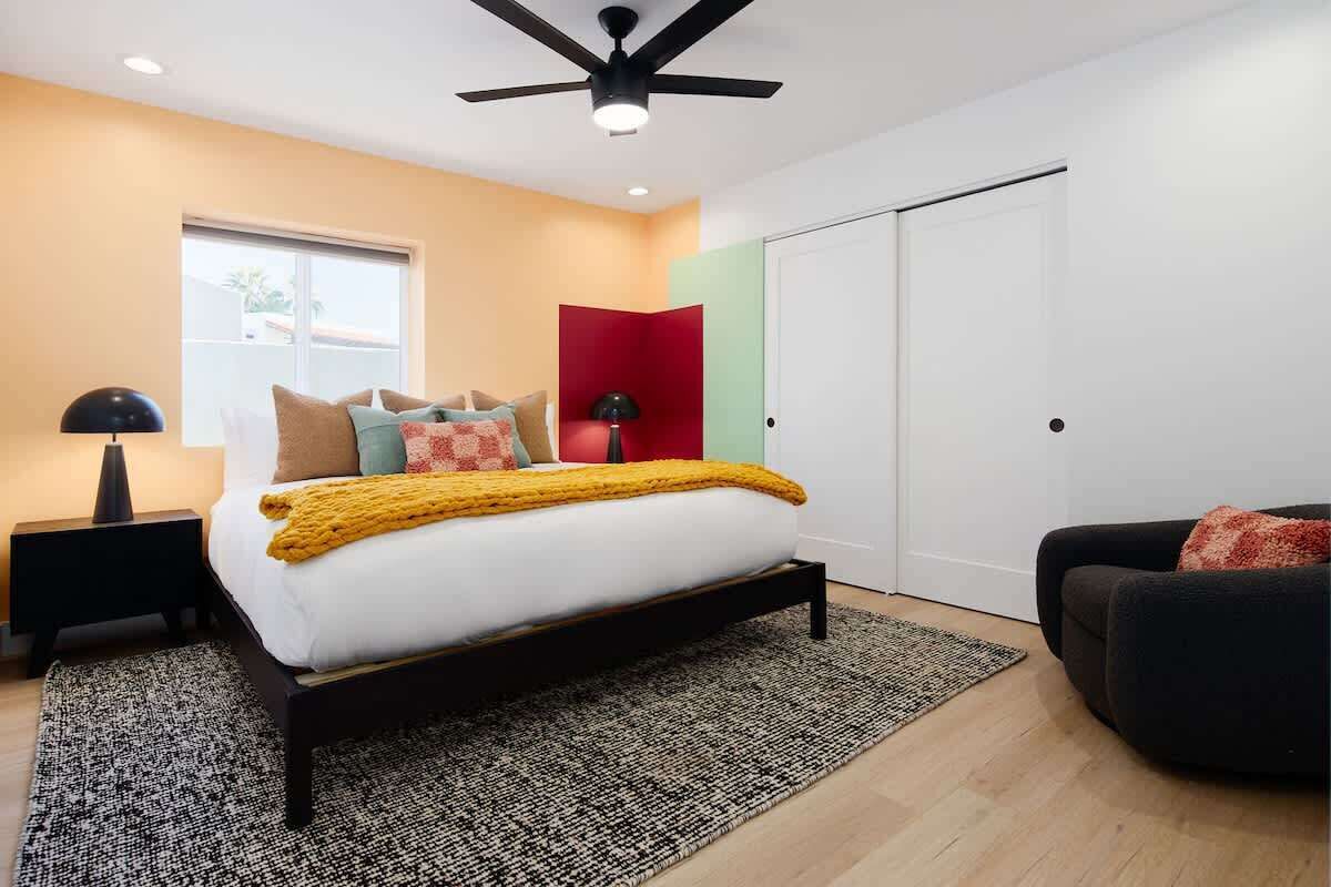 A bedroom with a bed, a ceiling fan, a nightstand, a lamp, a window, and a door.