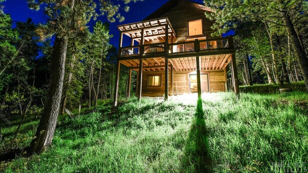 A wooden cabin with a balcony, surrounded by trees and set against a night sky. - Rustic 4 bedroom cabin at Gilded Mountain, wifi, pool access, paved roads (Lead)