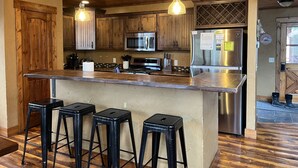 A kitchen with wooden cabinets, stainless steel appliances, and a bar area with stools. - Rustic 4 bedroom cabin at Gilded Mountain, wifi, pool access, paved roads (Lead)