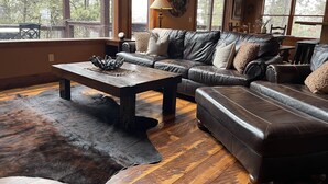 A cozy living room with a leather sofa, a wooden coffee table, and a fur rug. - Rustic 4 bedroom cabin at Gilded Mountain, wifi, pool access, paved roads (Lead)